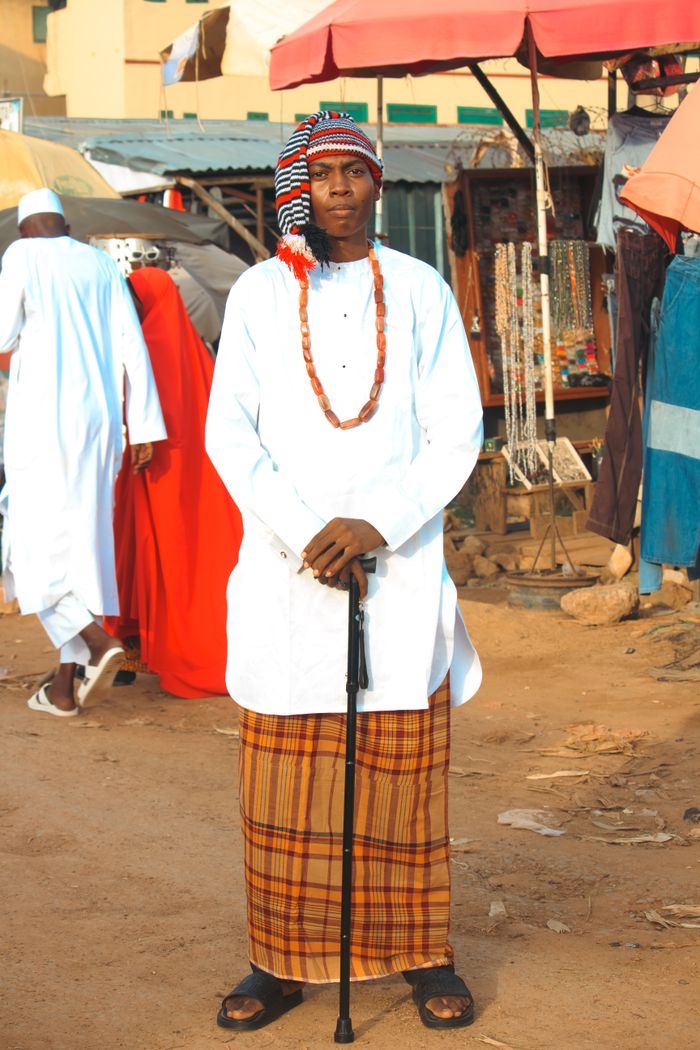 Services Man in traditional African clothing poses in a bustling market with cultural accessories.